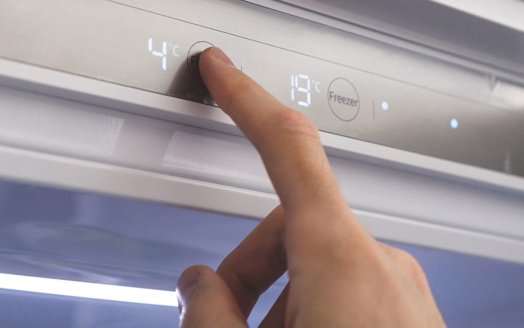 En person reglerar temperaturen i kylskåp och frys.