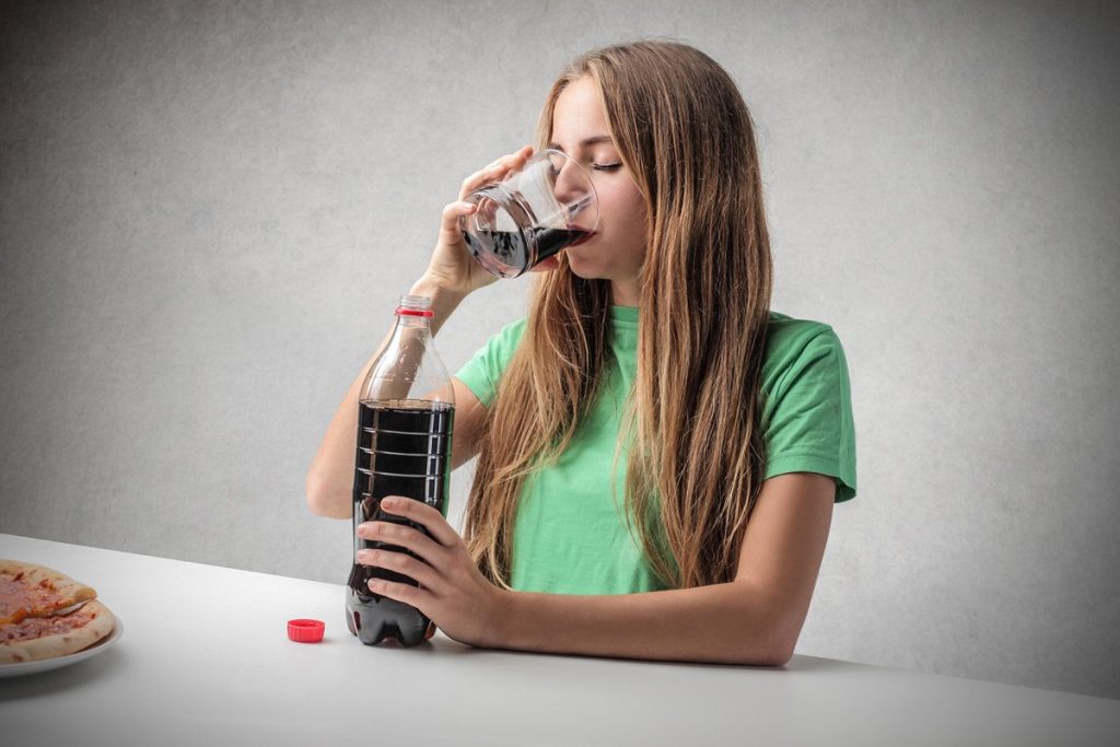 Flickan dricker Coca-Cola.