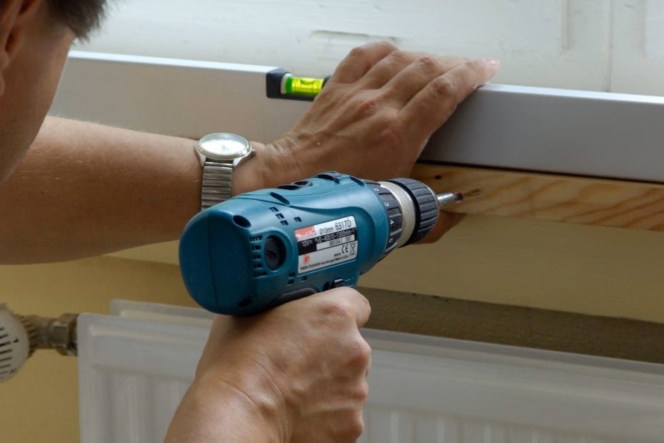 En man spikar fast en hylla ovanför elementet för att förbättra uppvärmning i huset.