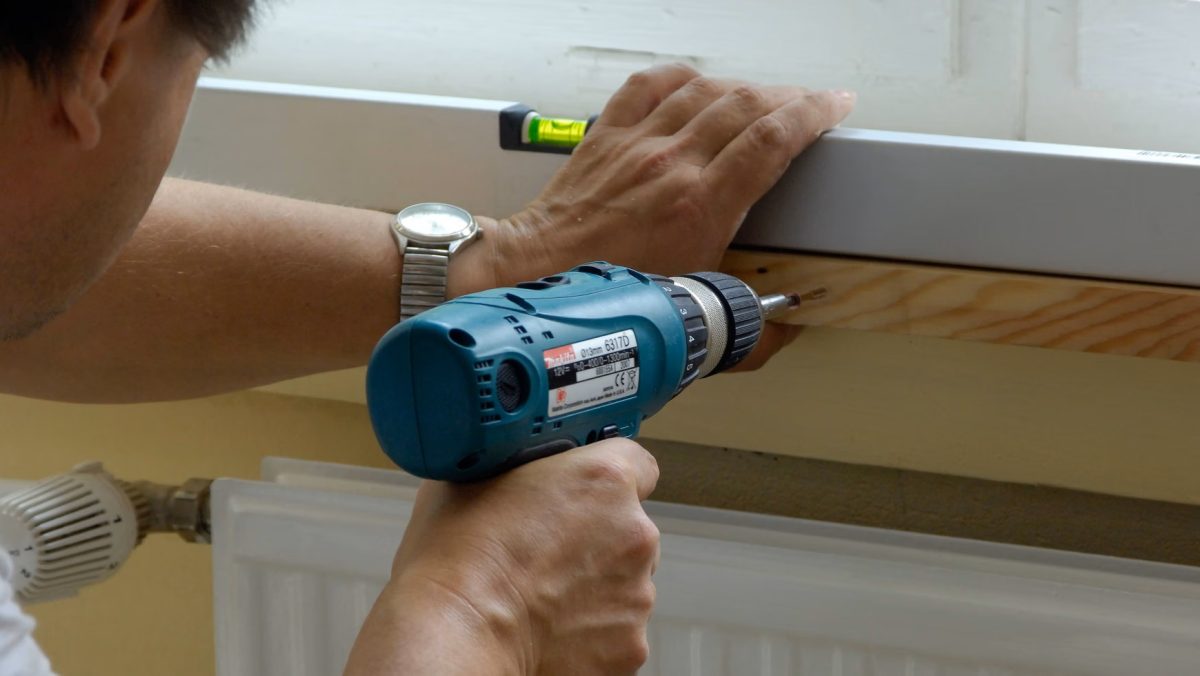 En man spikar fast en hylla ovanför elementet för att förbättra uppvärmning i huset.