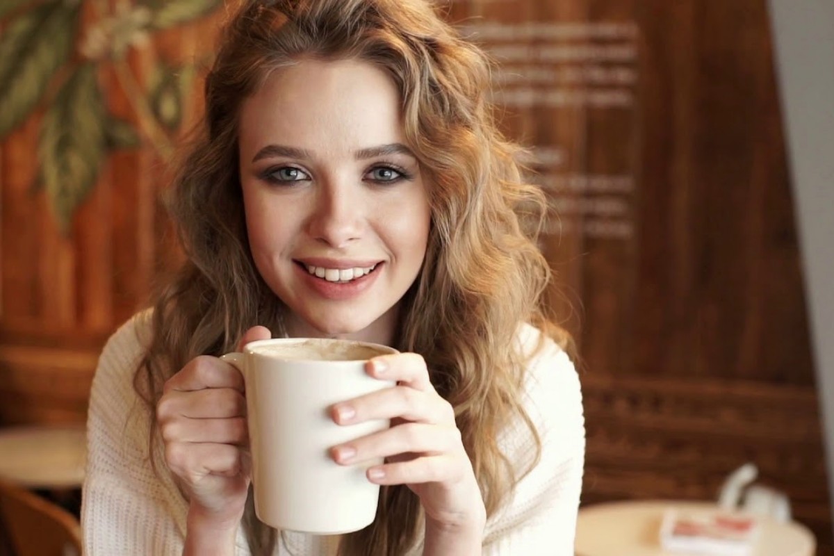 Flickan ler och dricker kaffe.