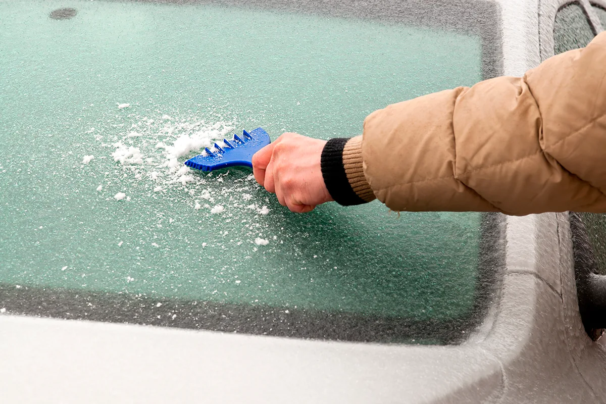 En man rengör den frusna vindrutan på en bil.